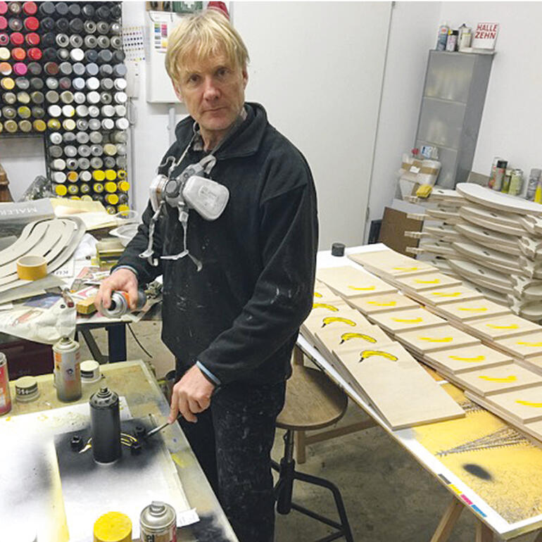Thomas Baumgärtel Mann in Atelier arbeitet mit Spraydosen an einem Holzbrett.