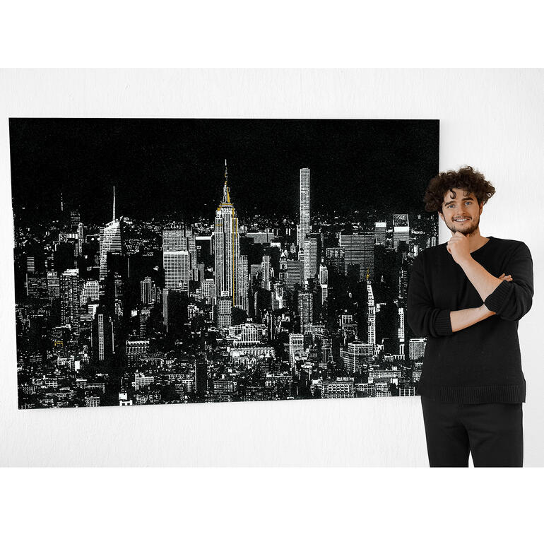 Tim Bengel Mann neben einem schwarz-weißen Bild der New Yorker Skyline mit beleuchteten Gebäuden.