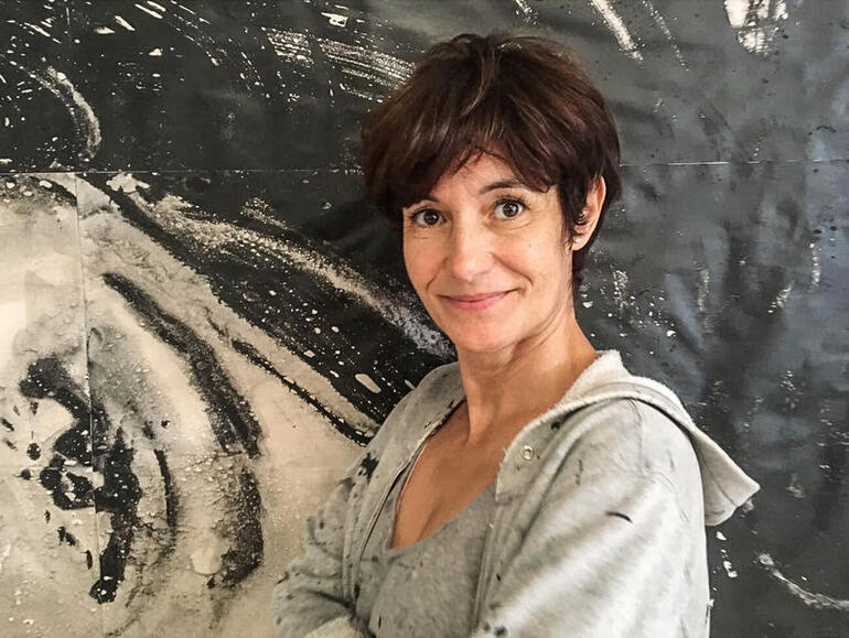 Lídia Masllorens Vilà Frau mit Kurzhaarschnitt lächelt vor einem abstrakten Kunstwerk.