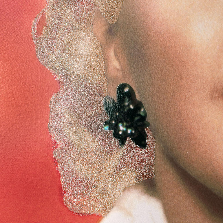 Detailaufnahme eines Ohrrings von Marilyn Monroe auf rotem Hintergrund.