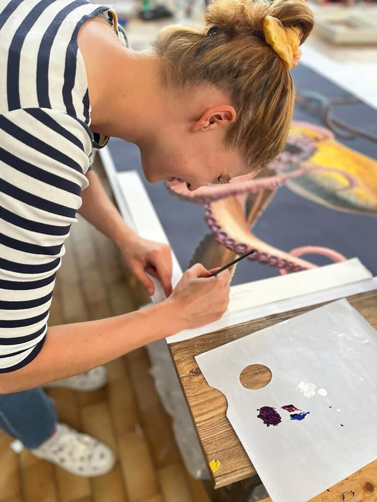 Lea Fricke in ihrem Atelier. Eine Künstlerin malt an einem großen Bild eines Oktopusses in einem Atelier.