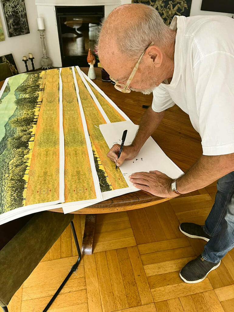 Ingo Wegerl bei der Signatur Mann signiert Kunstwerke in einem hellen Raum mit einem Tisch.