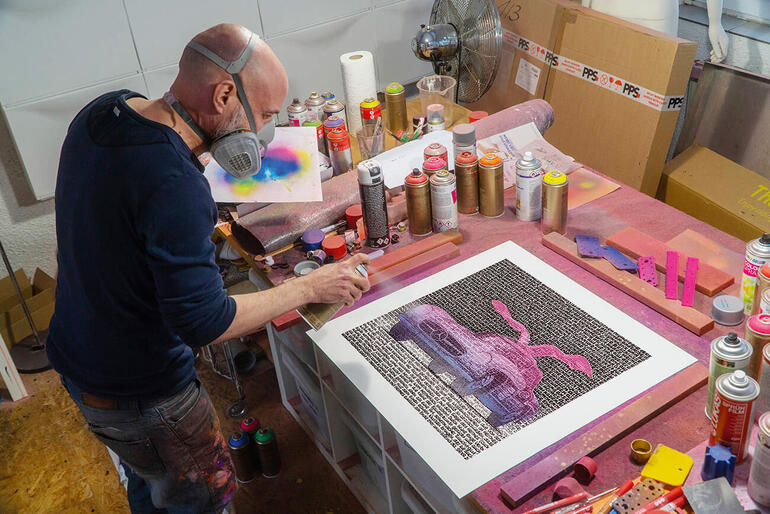 Künstler arbeitet an einem Bild, umgeben von verschiedenen Kunstmaterialien.
