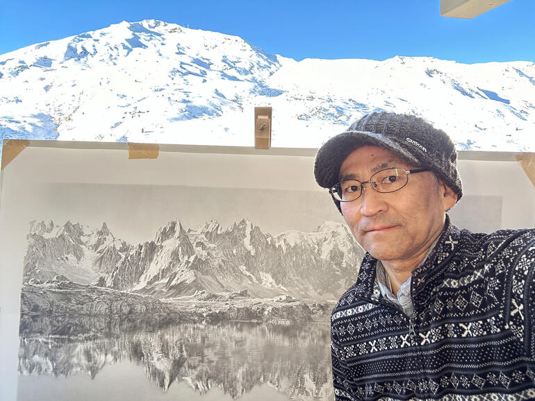 Koshi Takagi Der Künstler Koshi Takagi posiert vor einer Berglandschaft und seiner Zeichnung.