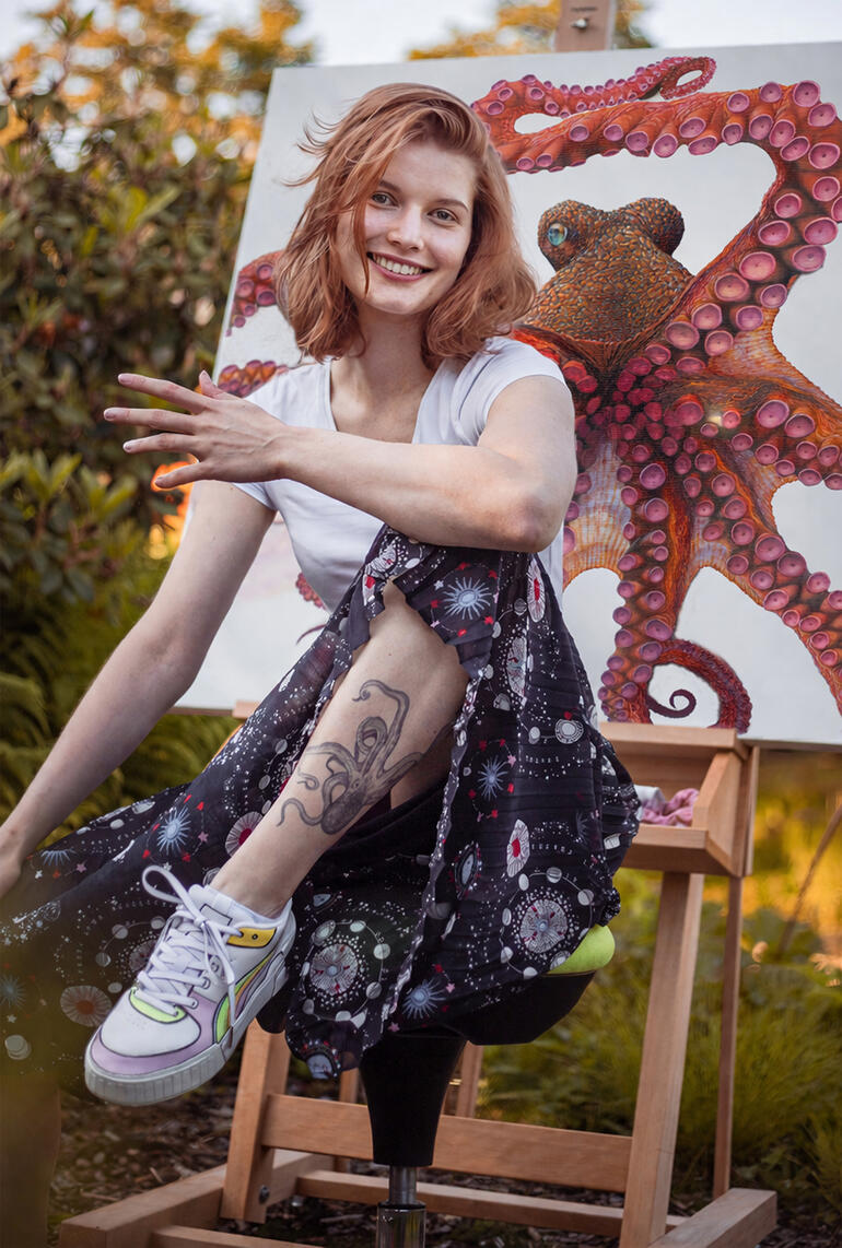 Frau mit langen Haaren in einem Atelier, posiert mit einem Bild eines Oktopus.
