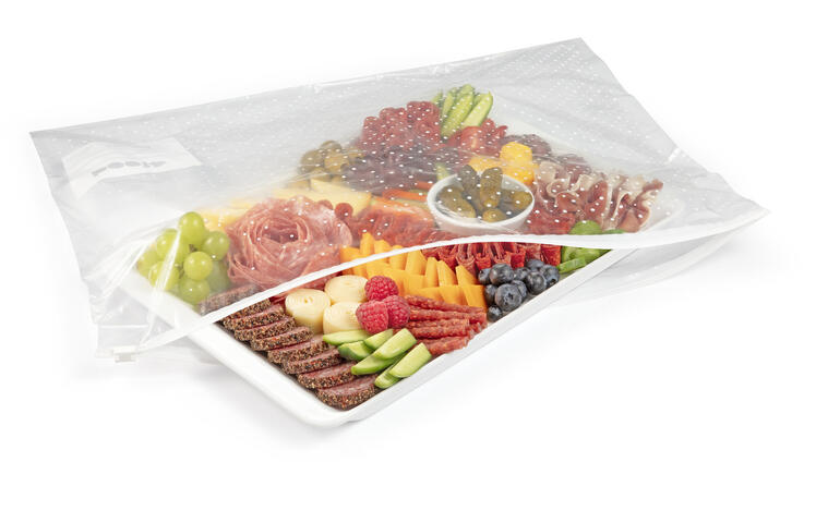 Bunte Platte mit verschiedenen Obst- und Wurststücken in Verpackung.
