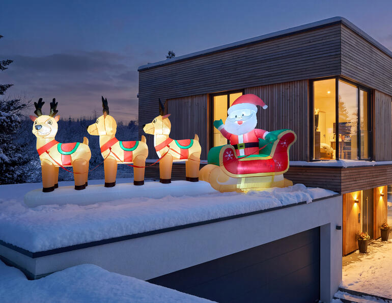 Aufblasbarer Rentierschlitten mit Santa Claus auf dem Dach eines modernen Hauses.