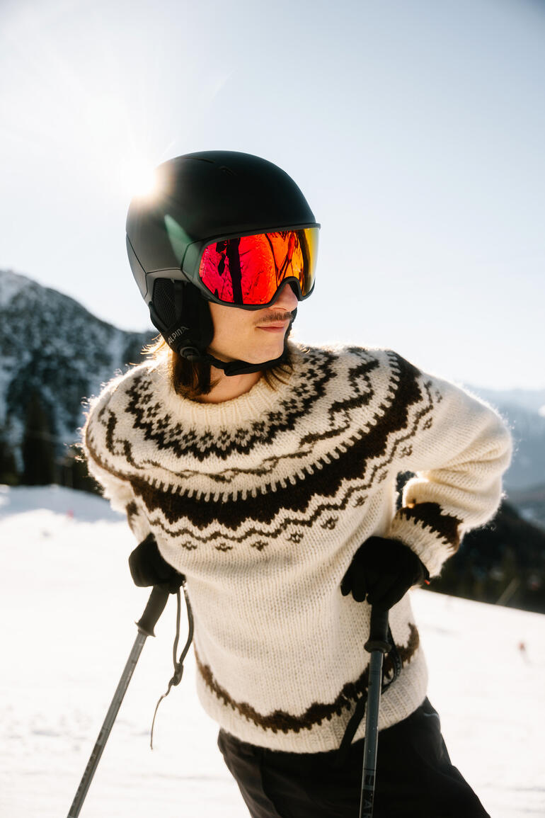 Person mit Hybrid-Visierhelm in Winterkleidung beim Skifahren in den Bergen.