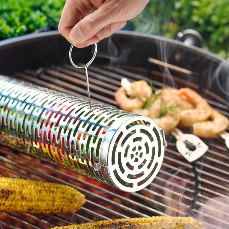 Hand zieht den Zylinder-Grillkorb vom Grill