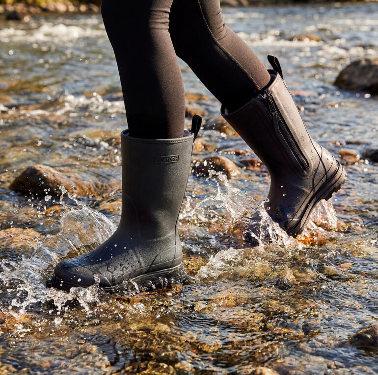 Gummistiefel in Schwarz an den Füßen einer Person im Wasser