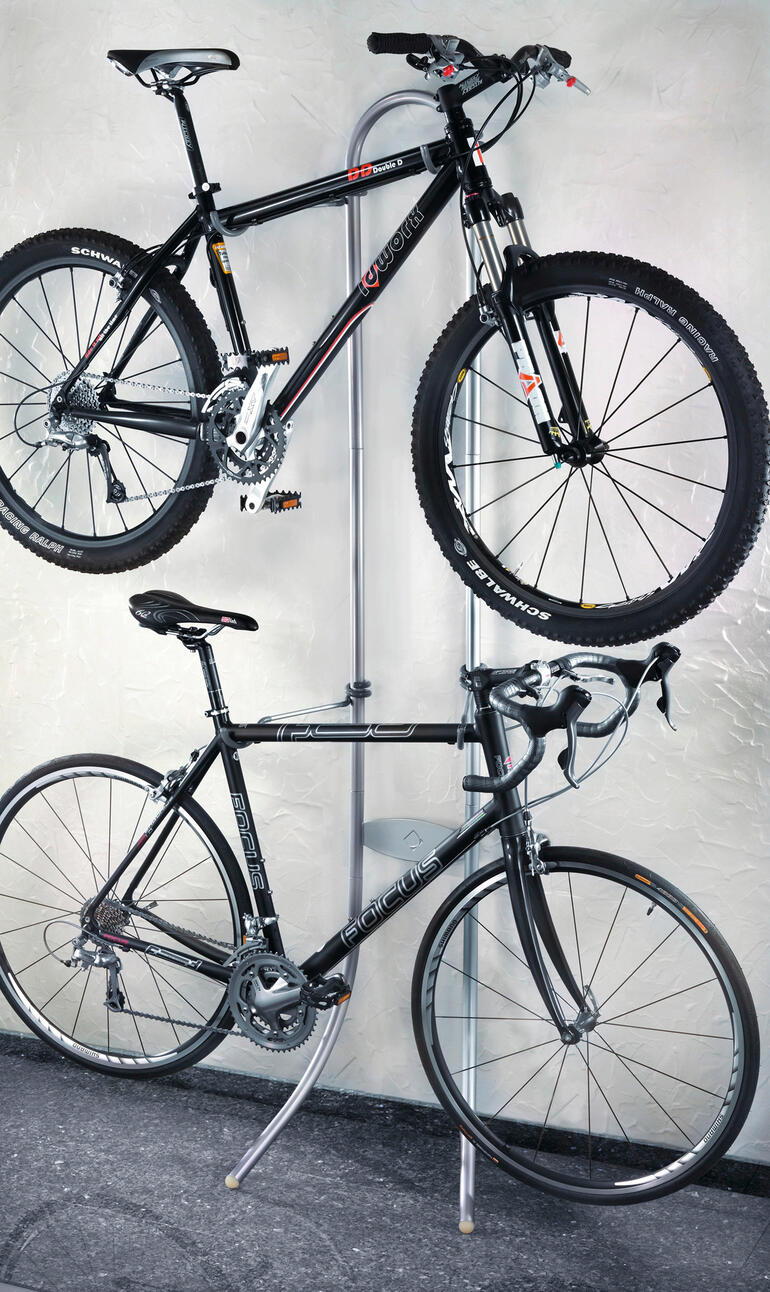 Zwei Fahrräder hängen an einem weißen Halter, einer ist ein Mountainbike.