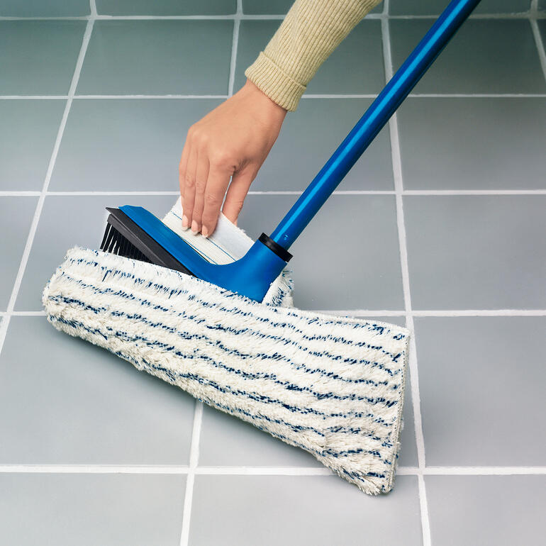 Der leicht aufziehbare Effektfaser-Wischbezug macht die Bodenreinigung perfekt. Hand hält einen V7-Besen beim Wischen über graue Fliesen.