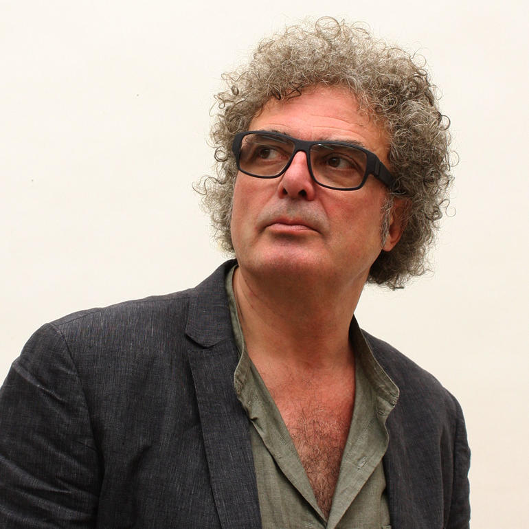 Jacinto Moros Mann mit lockigem Haar und Brille in einem grauen Blazer schaut nachdenklich zur Seite.