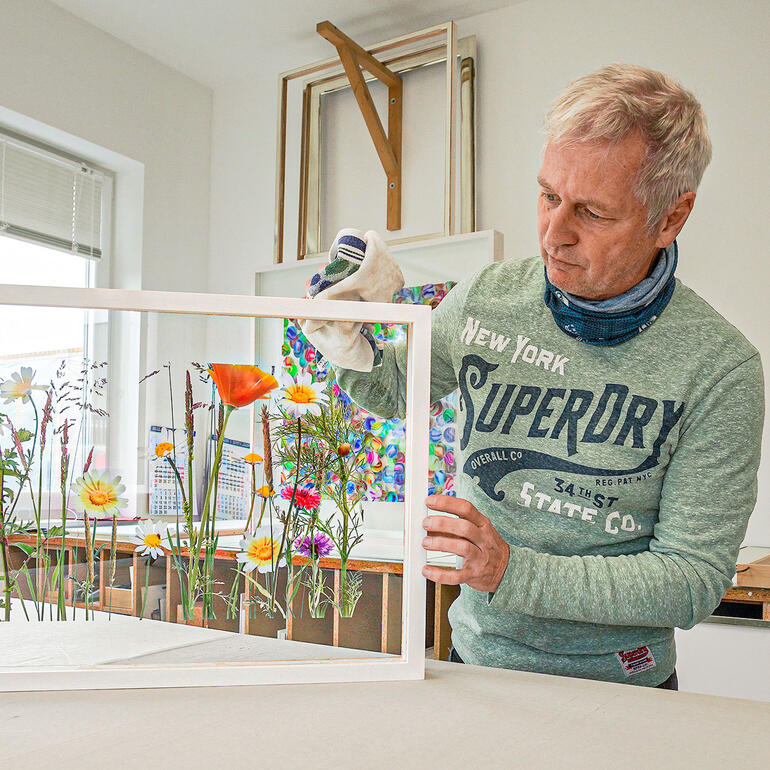 Andreas Lutherer Mann zeigt auf ein Bild mit Blumen im Hintergrund.