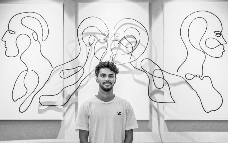 Mann steht vor Wand mit abstraktem Kunstwerk.