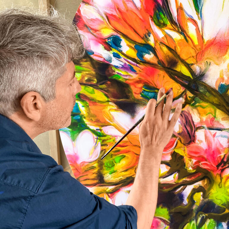 Armin Scheid koloriert jedes Exemplar partiell nach. Mann malt mit Pinsel an blühendem Kunstwerk.