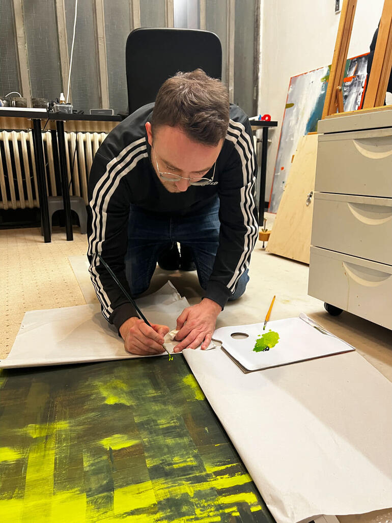 Michael Bajer Mann sitzt auf Boden, zeichnet mit Marker auf Papier.