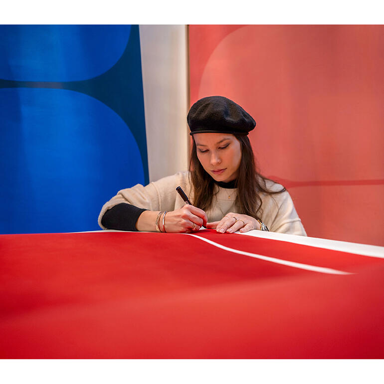 Lina Danitz skizziert auf rotem Papier in einer kreativen Umgebung.