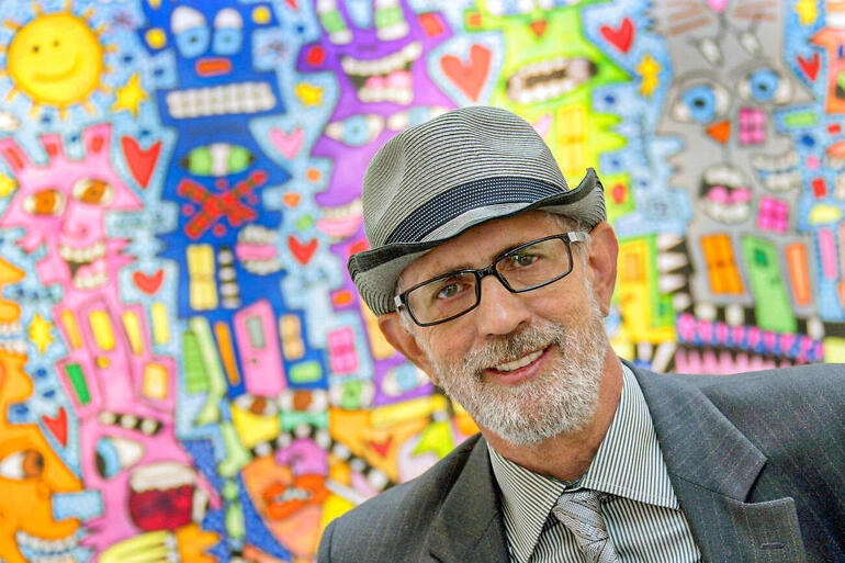 James Rizzi James Rizzi lächelt vor einem bunten Hintergrund mit lustigen Charakteren.