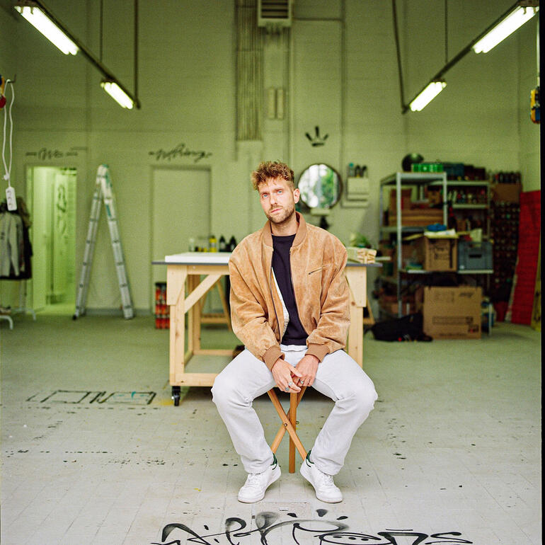 Steffen Mumm Steffen Mumm sitzt auf einem Stuhl in einem kreativen Atelier.