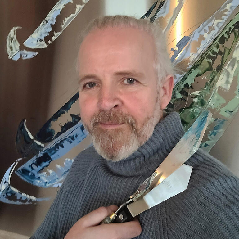 Paul La Poutré posiert mit einem Messer und einer künstlerischen Skulptur im Hintergrund.