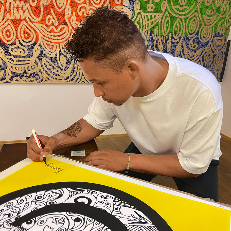 Romulo Kuranyi bei der Signatur seiner Edition. Romulo Kuranyi signiert ein großes Kunstwerk mit leuchtenden Farben.