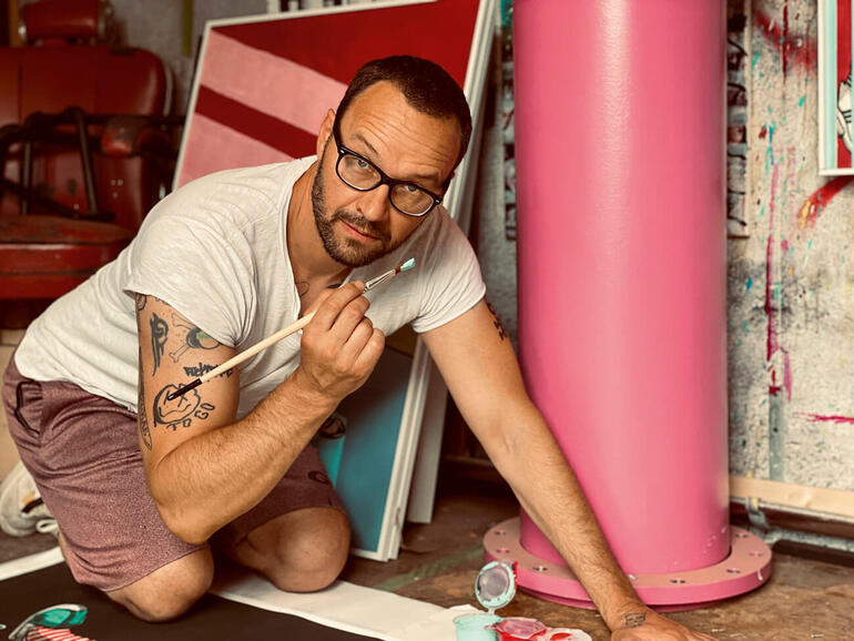 Ron Miller kniet und arbeitet an einem Kunstwerk mit einem Pinsel.