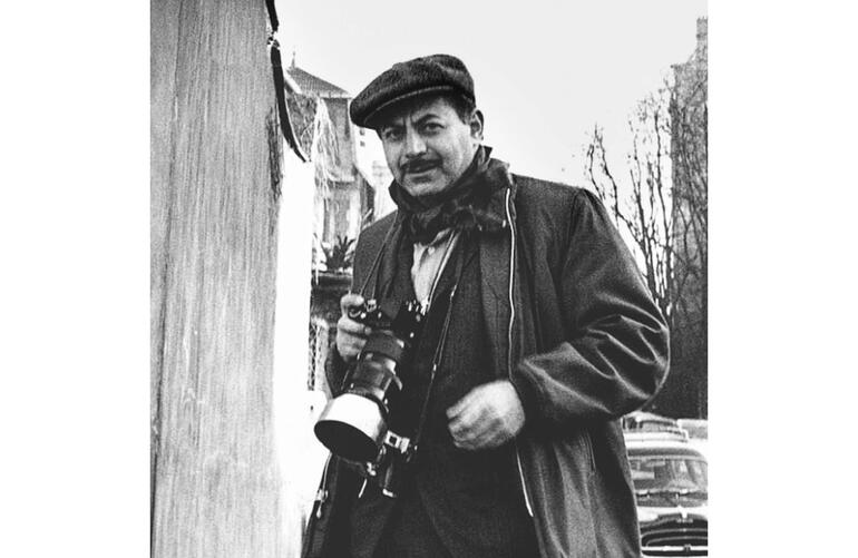 Sam Shaw Ein Fotograf mit einer Kamera in der Hand geht auf der Straße.