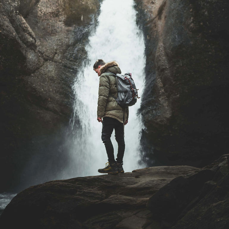 Marcel Siebert Marcel Siebert vor einem Wasserfall, trägt eine Winterjacke und hat einen Rucksack.